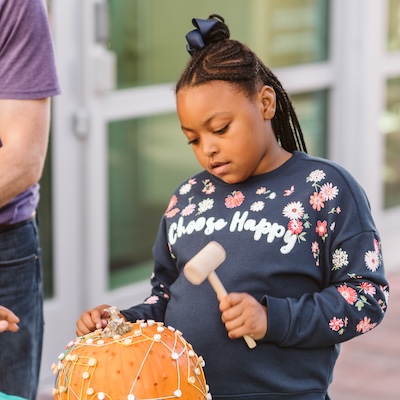 Little girl carving a pumpkin at fall festival.