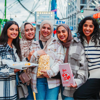 a group of friends in front of a ferris wheel carrying snacks at a carnival.